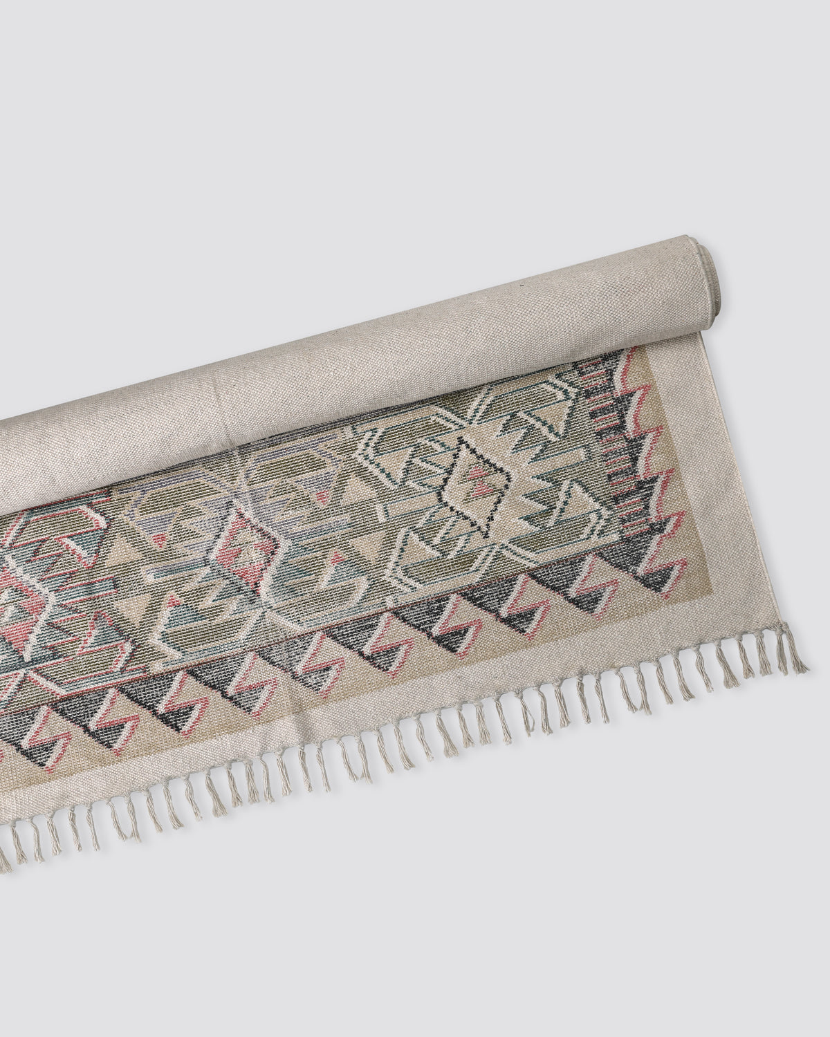 Block print cotton dhurrie rug half rolled, showing a pink and green geometric pattern