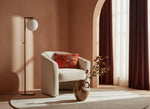 Orange bird print pillow on a cream boucle armchair beside a floor lamp