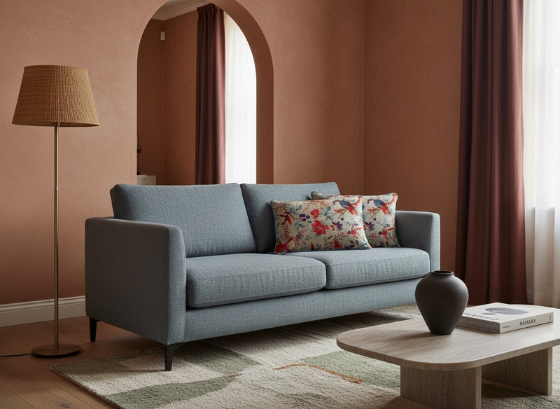 Beige bird print pillows on a grey-blue sofa in a warm terracotta room