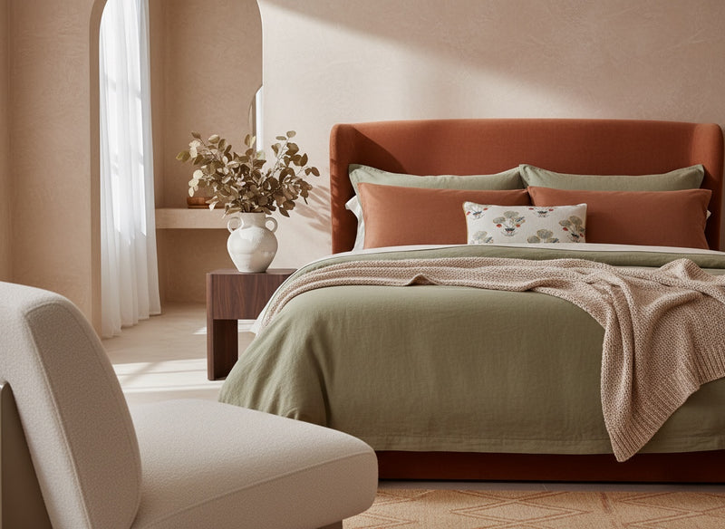 White floral print pillow on a sage green bed against a rust headboard