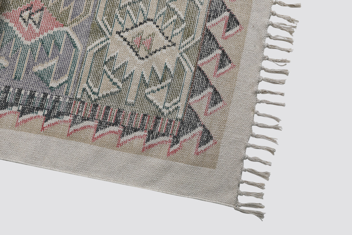 Close view of the dhurrie's geometric border in pink, grey and green with fringe