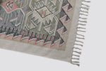 Close view of the dhurrie's geometric border in pink, grey and green with fringe