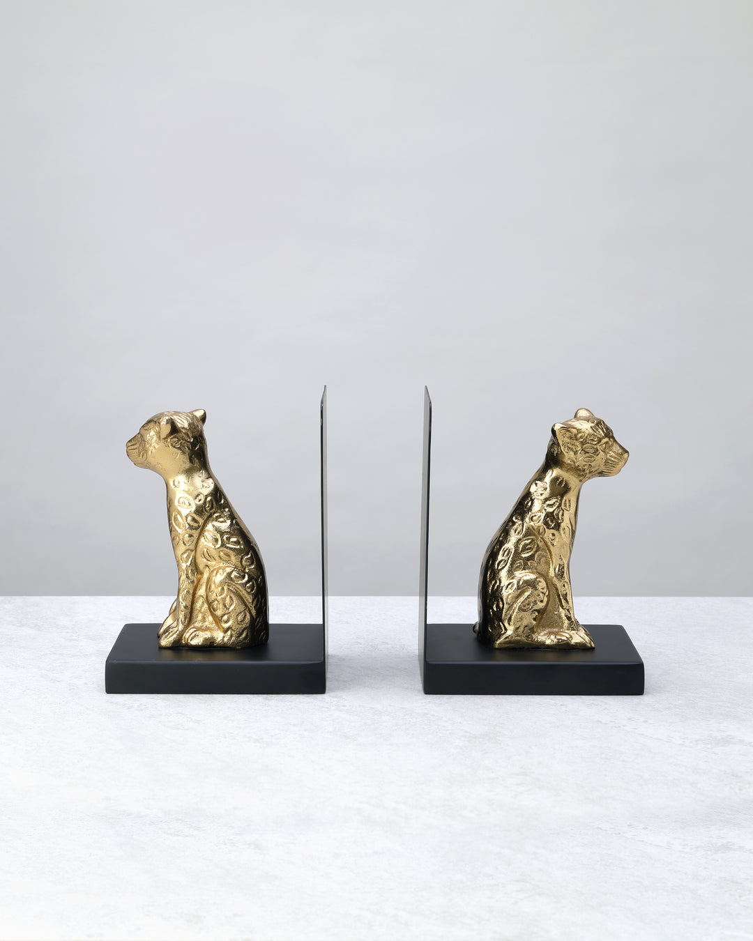 Pair of gold leopard bookends on black bases facing each other, on white