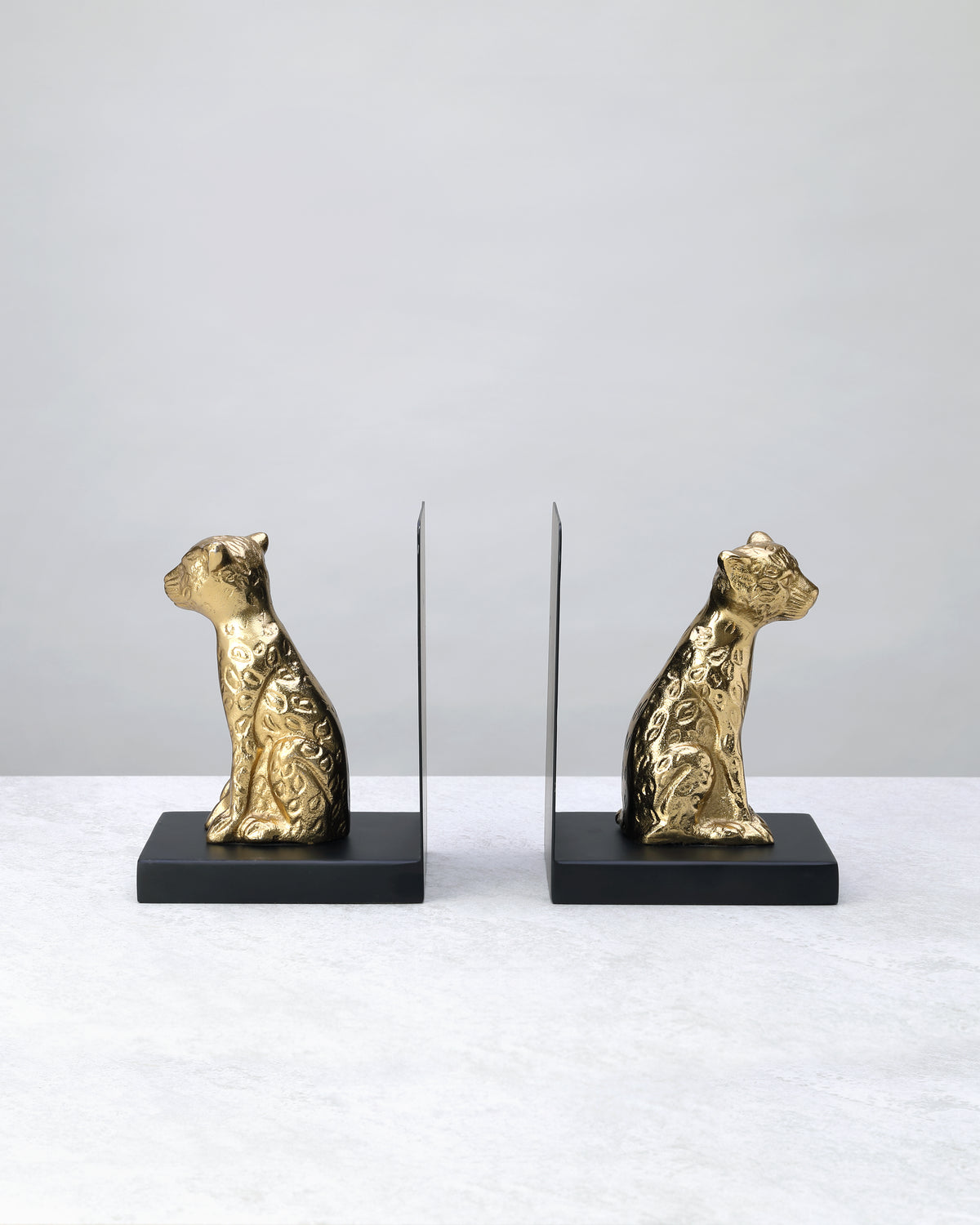 Pair of gold leopard bookends on black bases facing each other, on white