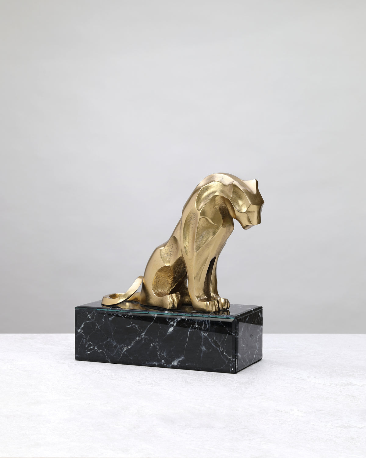 Gold lion figure seated on a black marble-finish base, on white