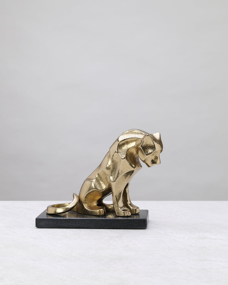 Gold lion figure crouching on a black marble base, side view on white
