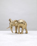 Gold elephant figure with a textured body and trunk lowered, side view on white