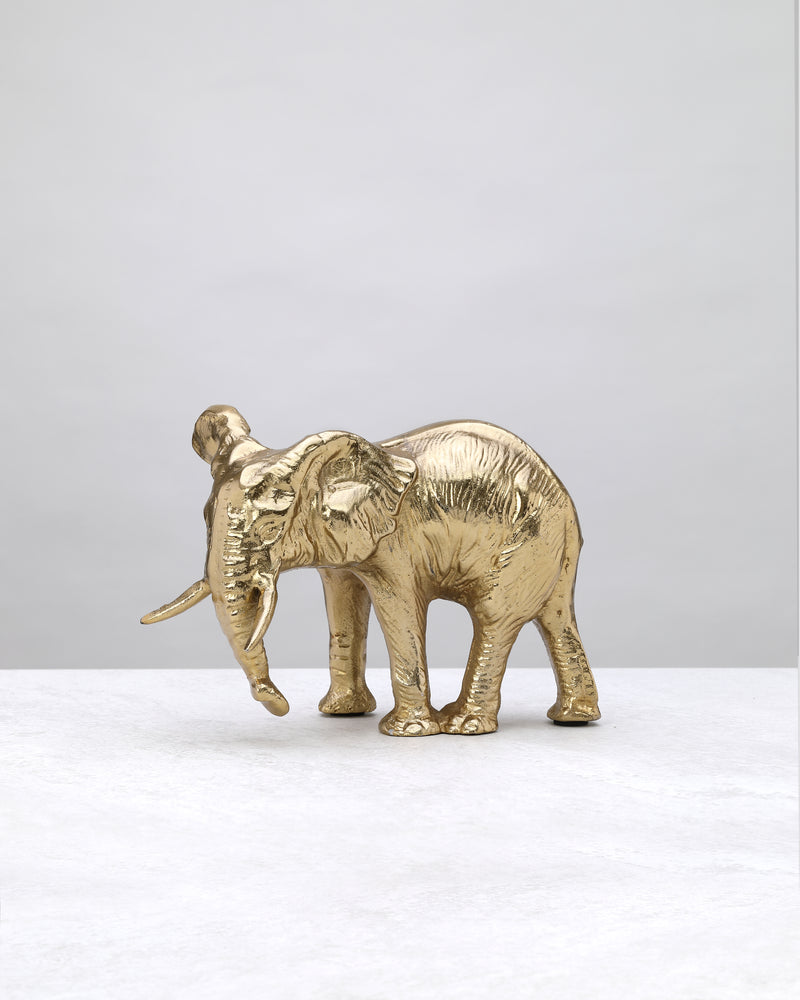 Gold elephant figure with a textured body and trunk lowered, side view on white