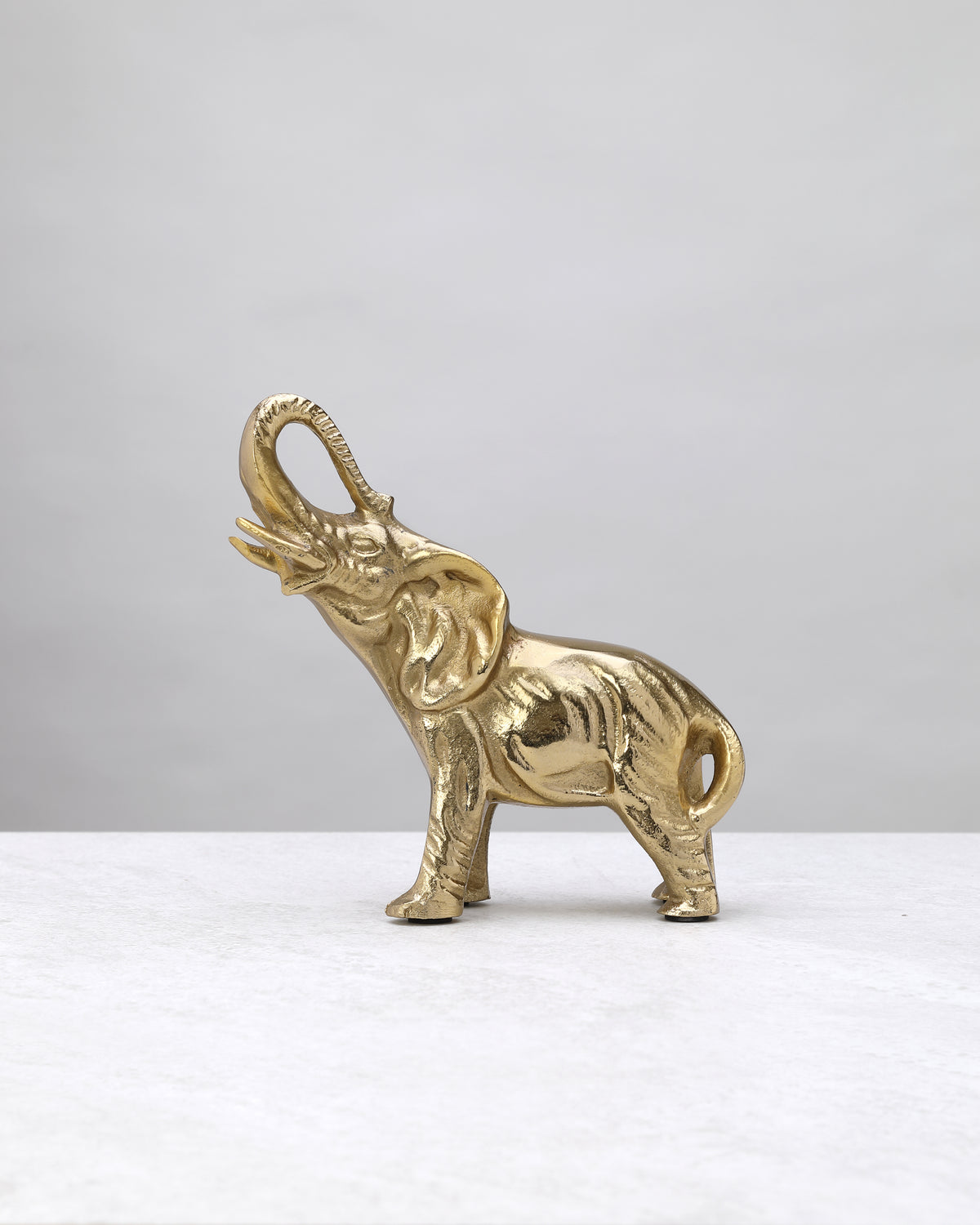 Petite gold elephant figure with a raised trunk and textured body, side view