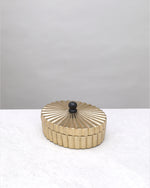 Small gold fluted keepsake box closed, showing the ribbed lid and black knob