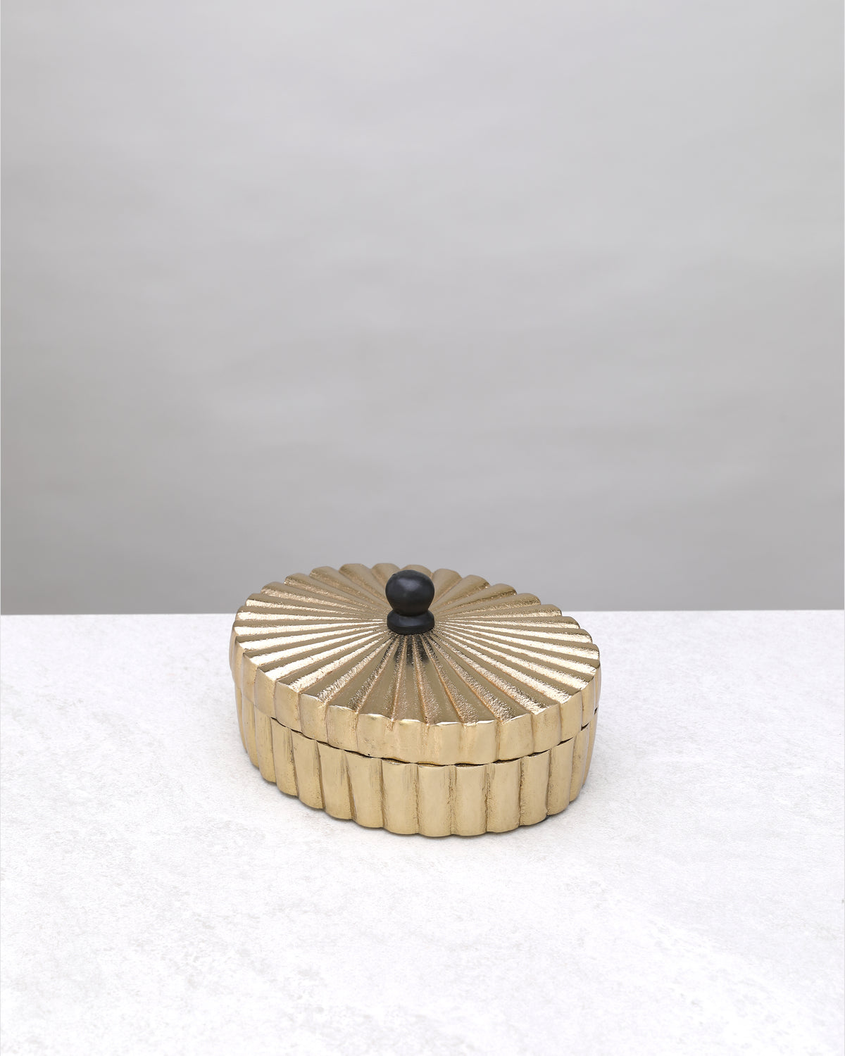 Small gold fluted keepsake box closed, showing the ribbed lid and black knob