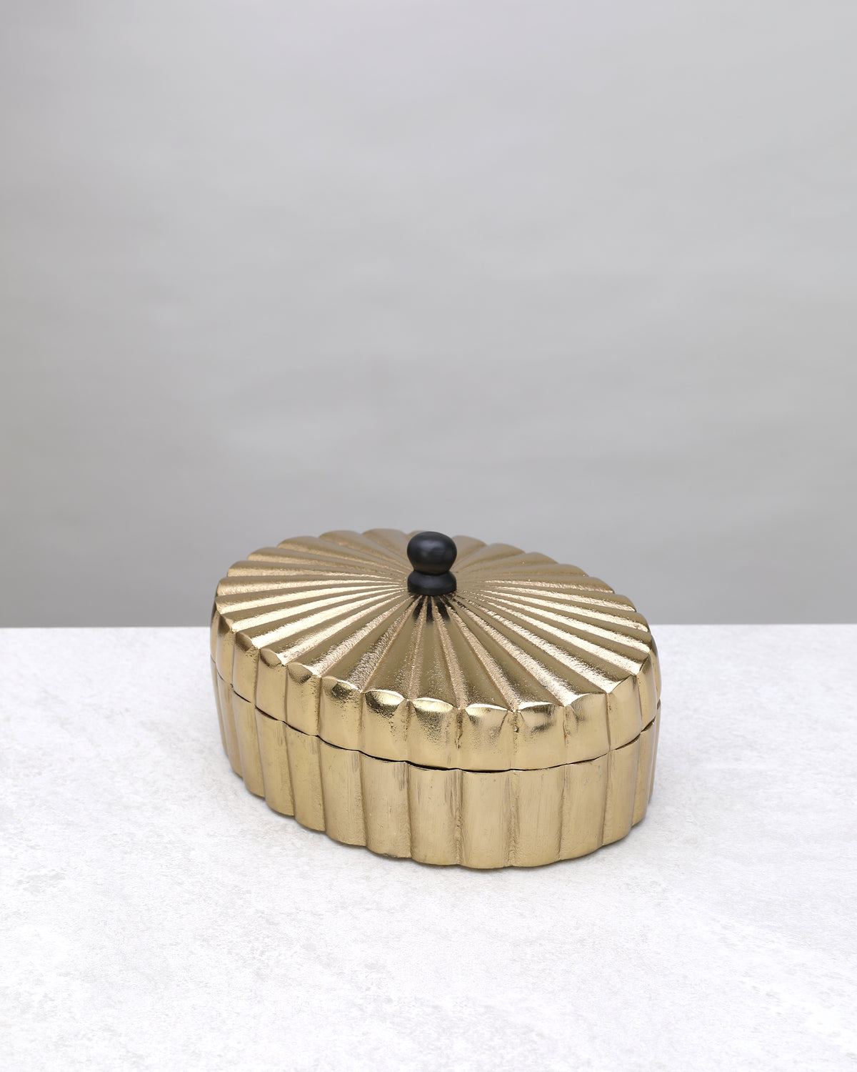 Large gold oval keepsake box closed, showing the fluted sides and black knob
