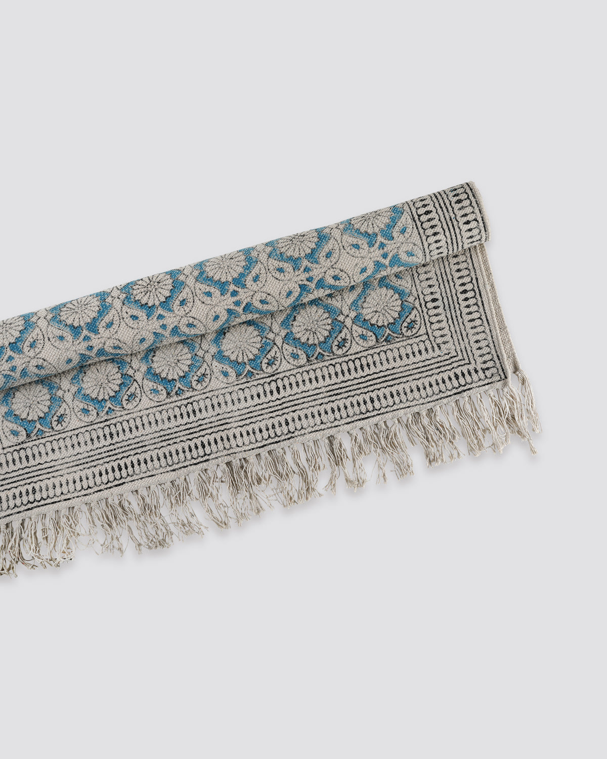 Teal block print cotton dhurrie rug folded to show the pattern and fringed ends