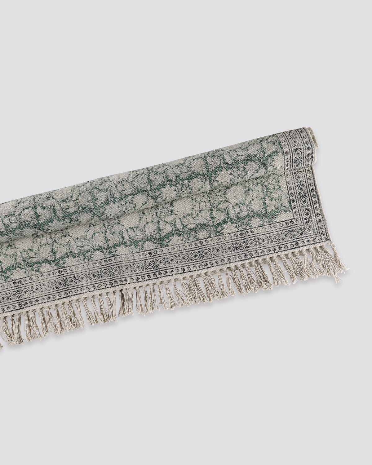 Green block print cotton dhurrie rug folded, showing the printed pattern and fringe