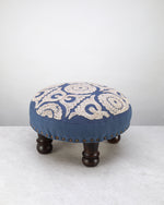 Blue round foot stool with a cream embroidered medallion top on dark wooden legs