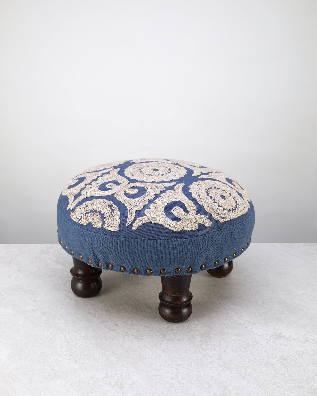 Blue round foot stool with a cream embroidered medallion top on dark wooden legs