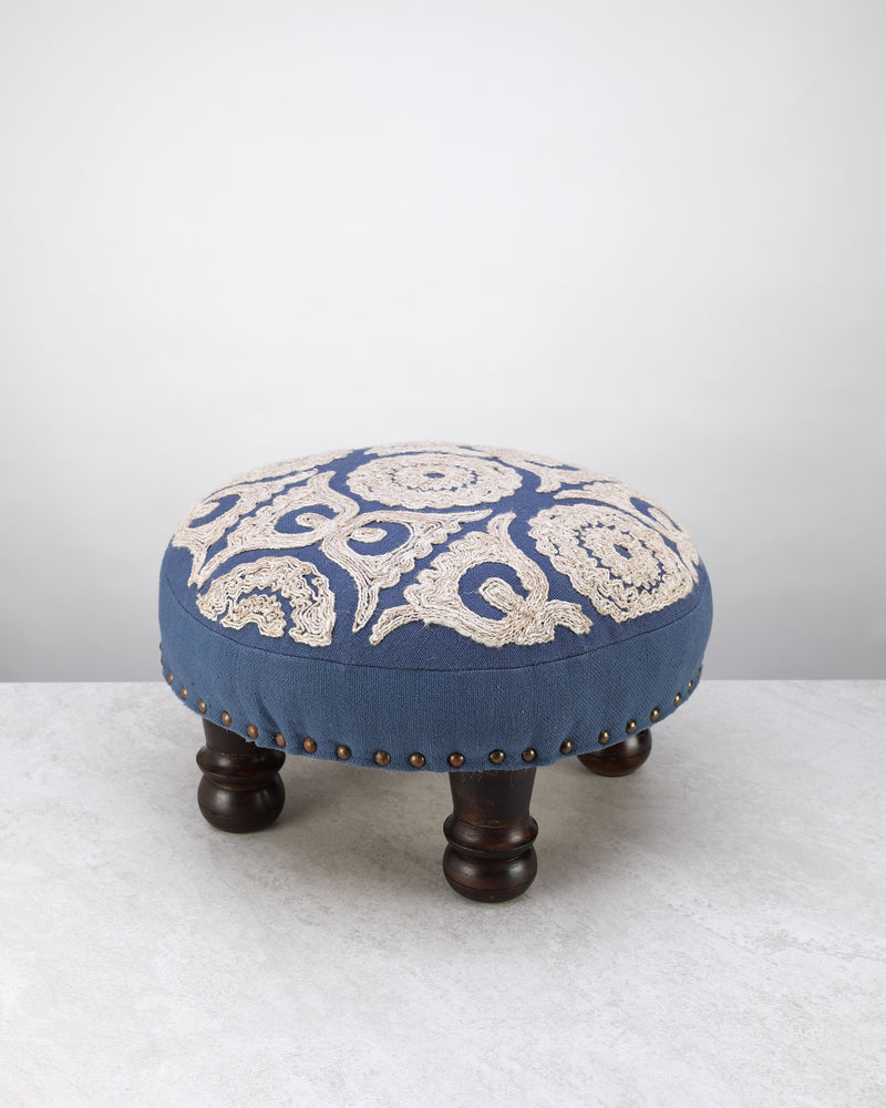 Blue round foot stool with a cream embroidered medallion top on dark wooden legs