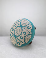 Teal Dori foot stool tipped on its side to show the embroidered top and studded edge