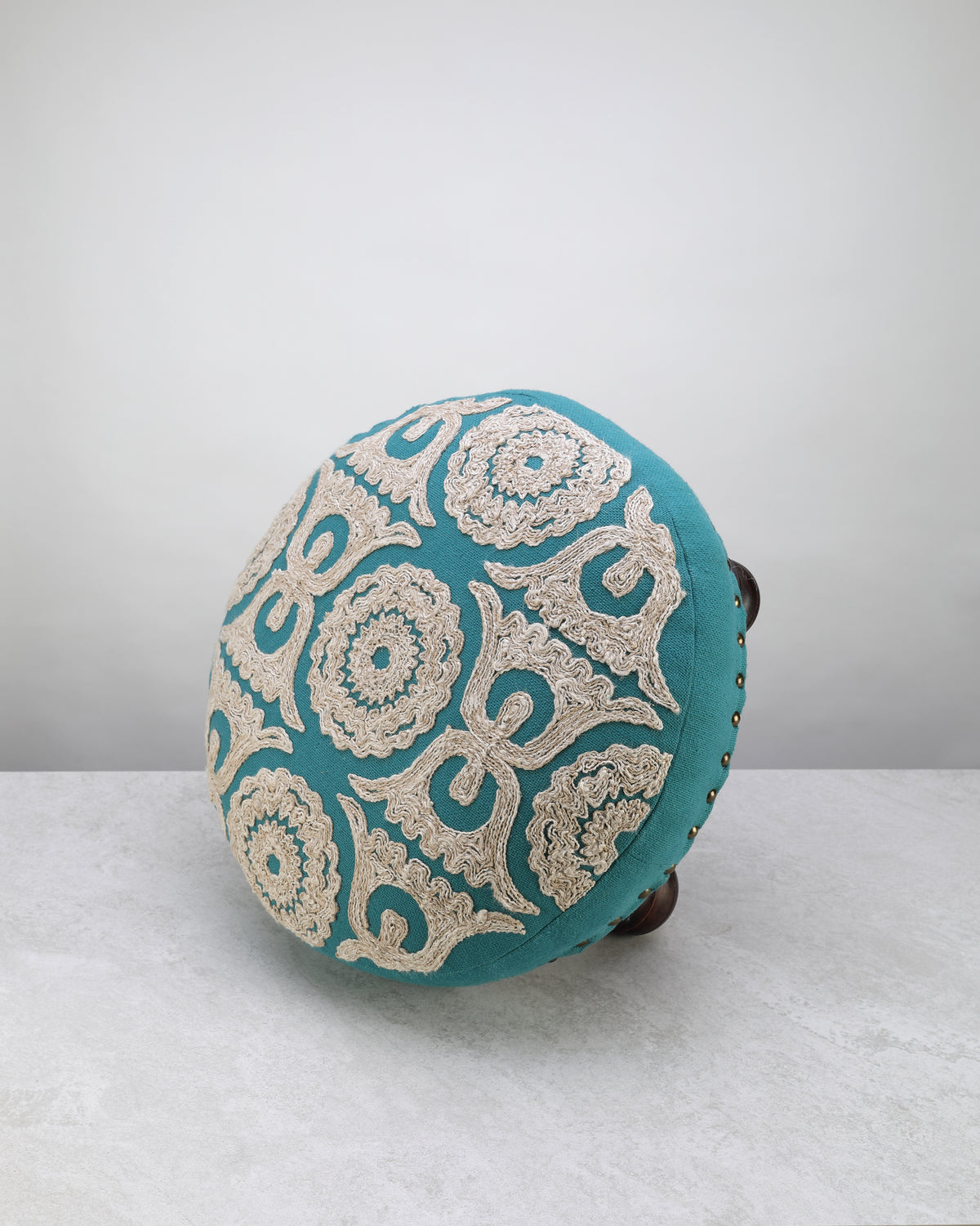 Teal Dori foot stool tipped on its side to show the embroidered top and studded edge