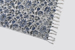 Corner of the blue floral dhurrie showing the print and tasselled fringe
