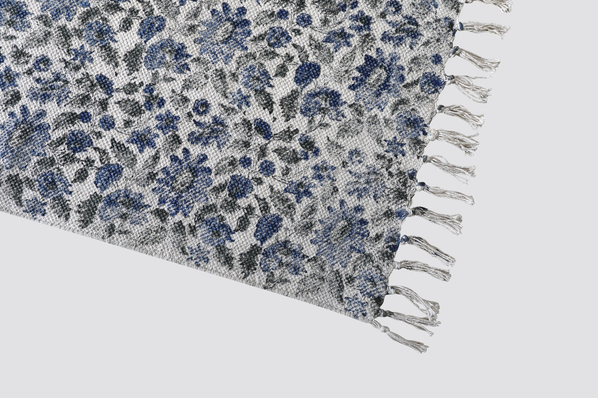 Corner of the blue floral dhurrie showing the print and tasselled fringe