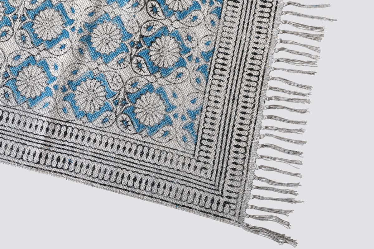 Corner of the teal block print dhurrie showing the border and tasselled fringe