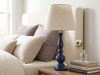Deep blue Dusk mango wood table lamp on a bedside table beside grey cushions and books