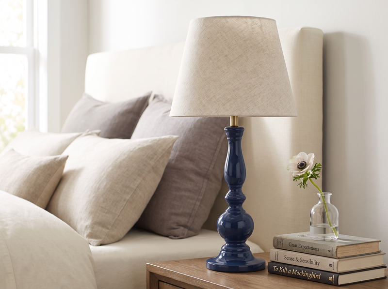 Deep blue Dusk mango wood table lamp on a bedside table beside grey cushions and books