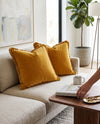 Mustard fringed velvet cushions on a grey sofa, a hand setting down a cup