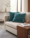 Two teal piped velvet cushions on a cream sofa beside a wooden coffee table