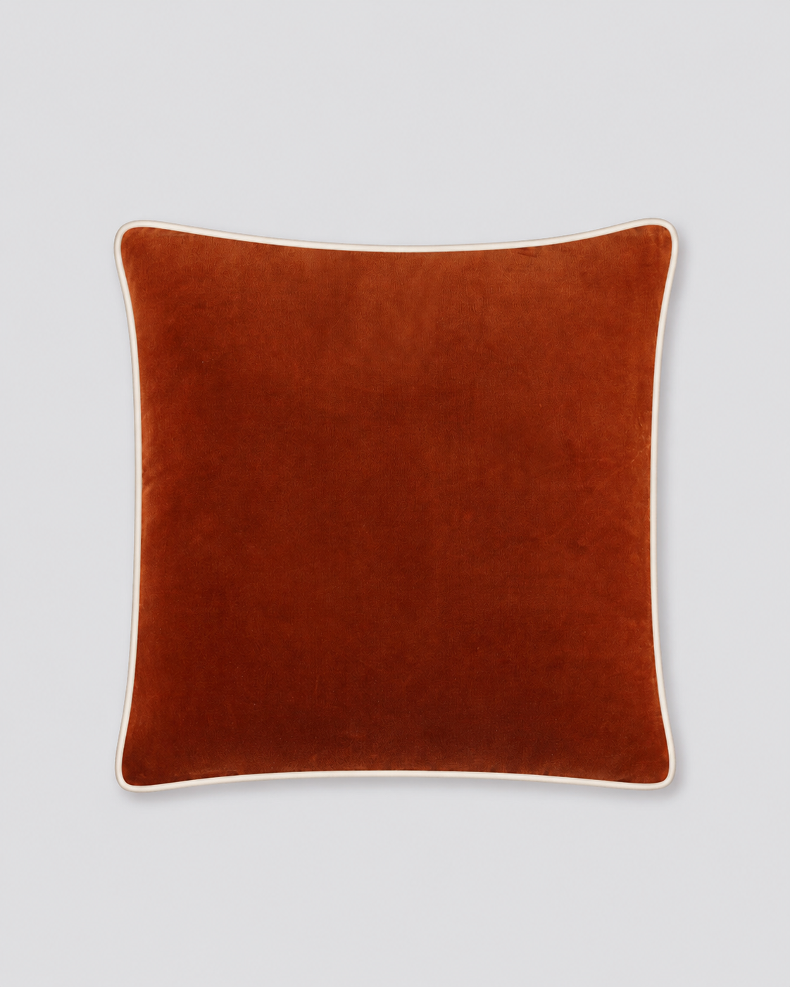 Rust velvet cushion cover with cream piping around the edge, front view