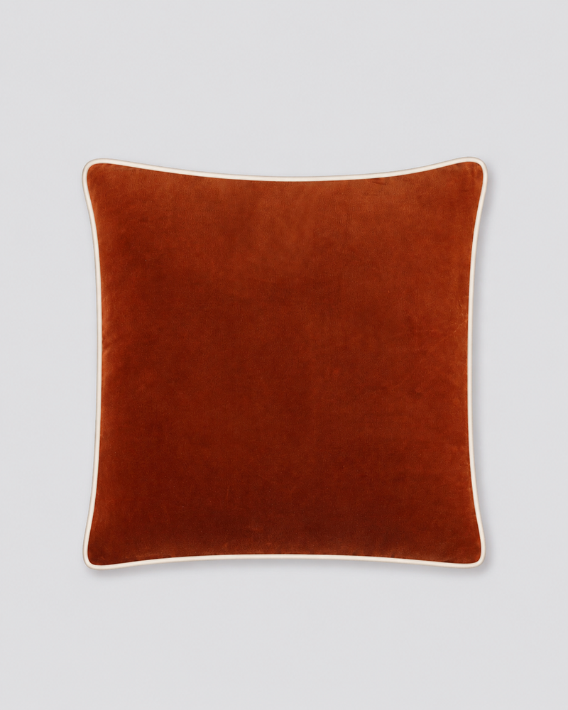 Rust velvet cushion cover with cream piping around the edge, front view
