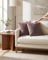 Dusty pink piped velvet cushions on a cream sofa, a hand plumping one