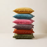 Stack of fringed velvet cushions in mustard, blue, pink, mauve, rust and olive