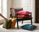 Mustard piped velvet cushion leaning on a cane chair with olive, pink and teal cushions