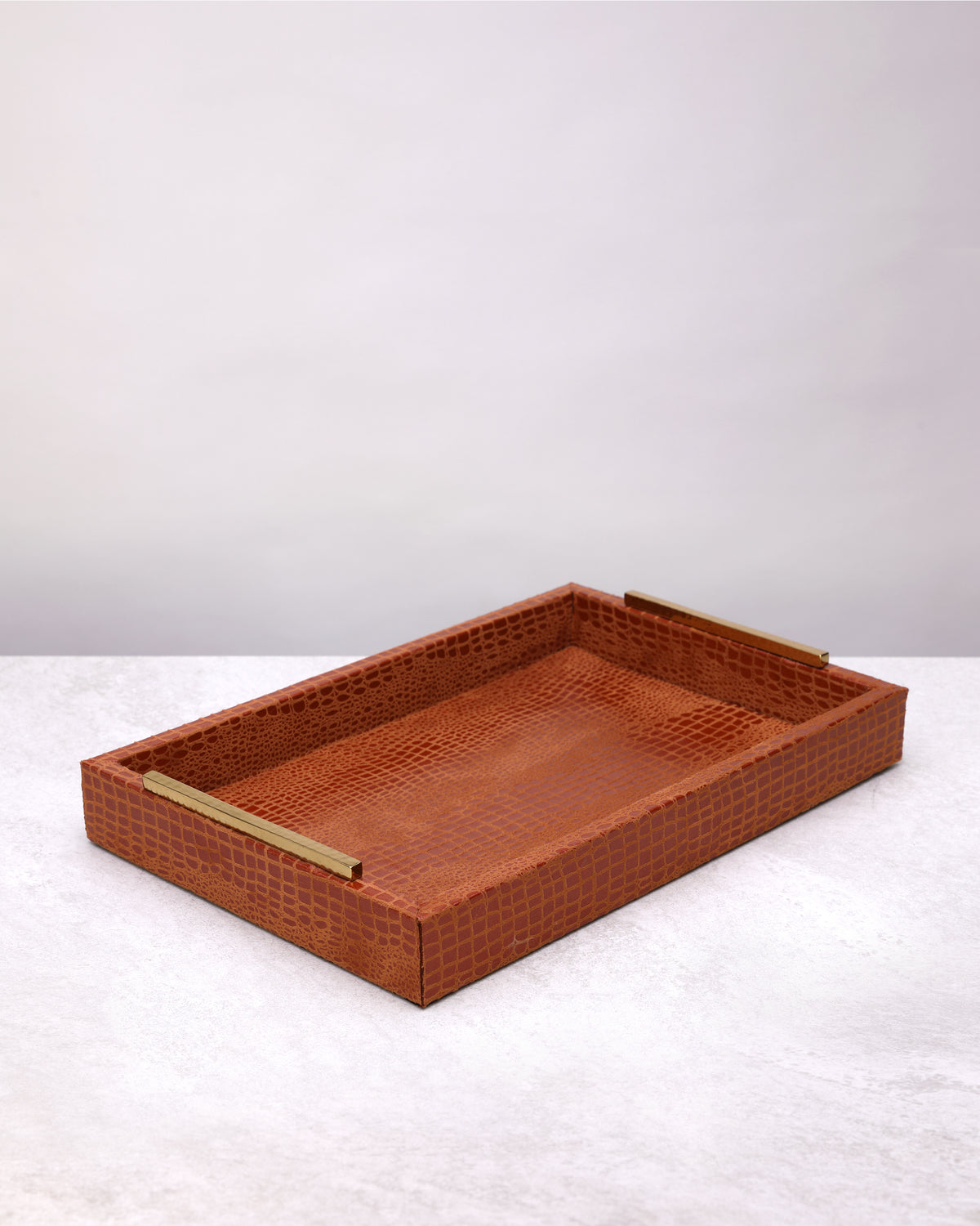 Small tan croc-textured faux leather tray with brass handles, on white