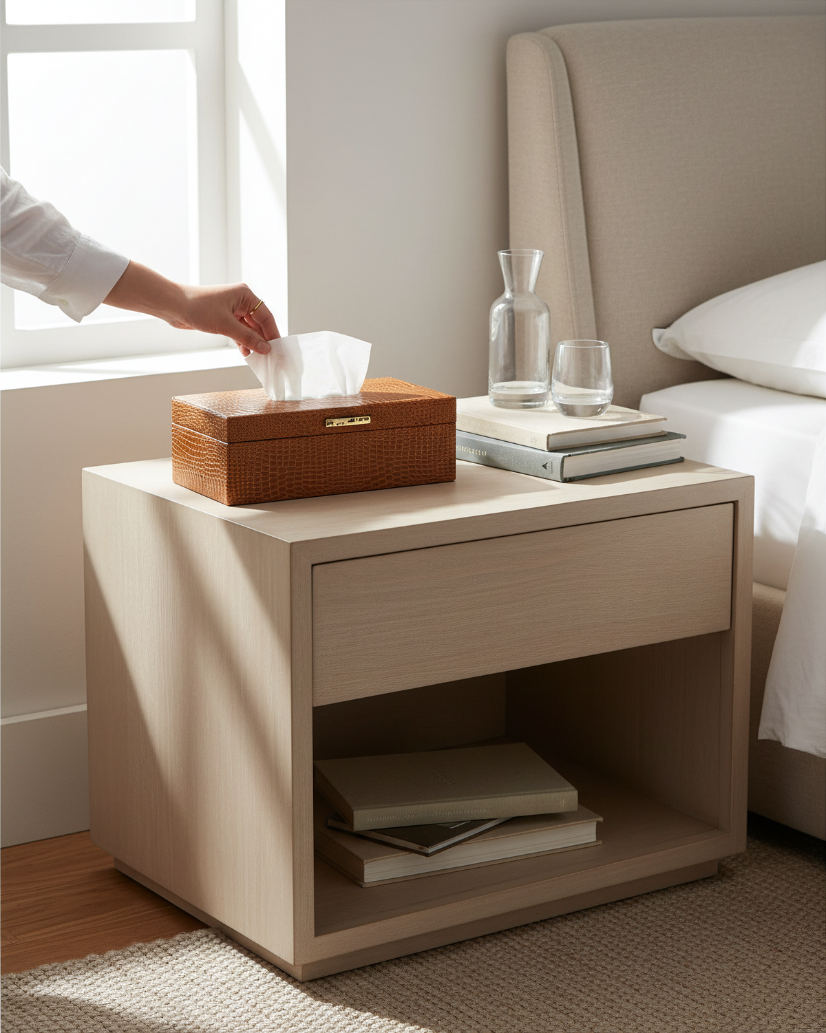 Tan faux leather tissue box on a bedside table, a hand pulling a tissue