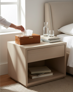 Tan faux leather tissue box on a bedside table, a hand pulling a tissue