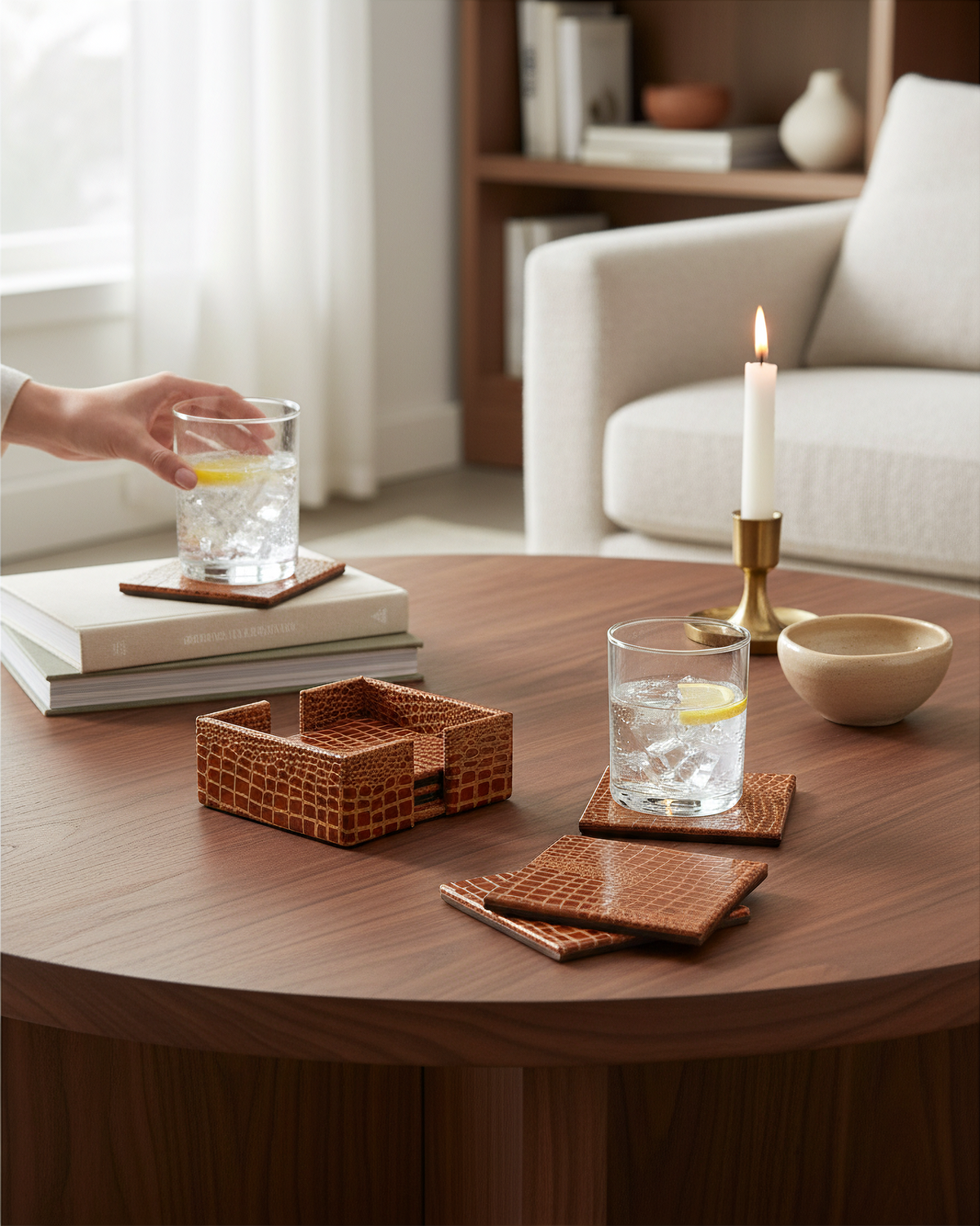 Hand setting a glass on a tan faux leather coaster on a round wooden table