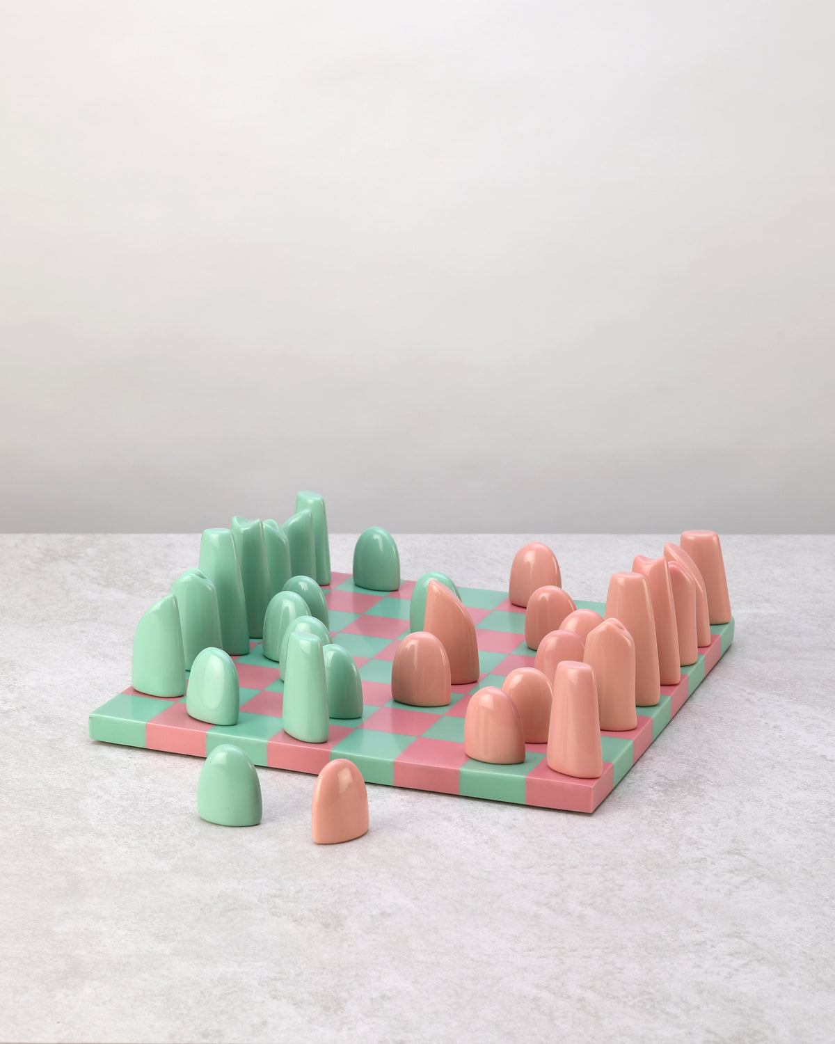 Cast resin chess board in pink and mint green checks with rounded pieces, angled view