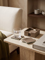 Pea green faux leather coasters and holder on a marble side table beside a glass