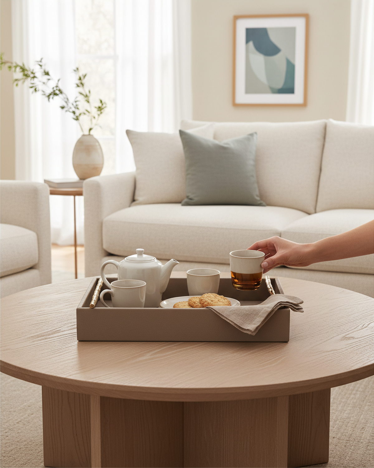 Small pea green faux leather tray on a round table with a teapot and cups, a hand lifting a cup