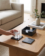 Navy blue faux leather coasters on a wooden coffee table, a hand setting down a glass