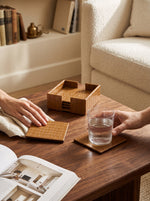 Hand setting a glass on a beige faux leather coaster on a wooden coffee table