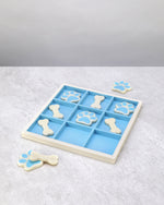 Resin tic-tac-toe board with spare bone and paw pieces beside it, angled view