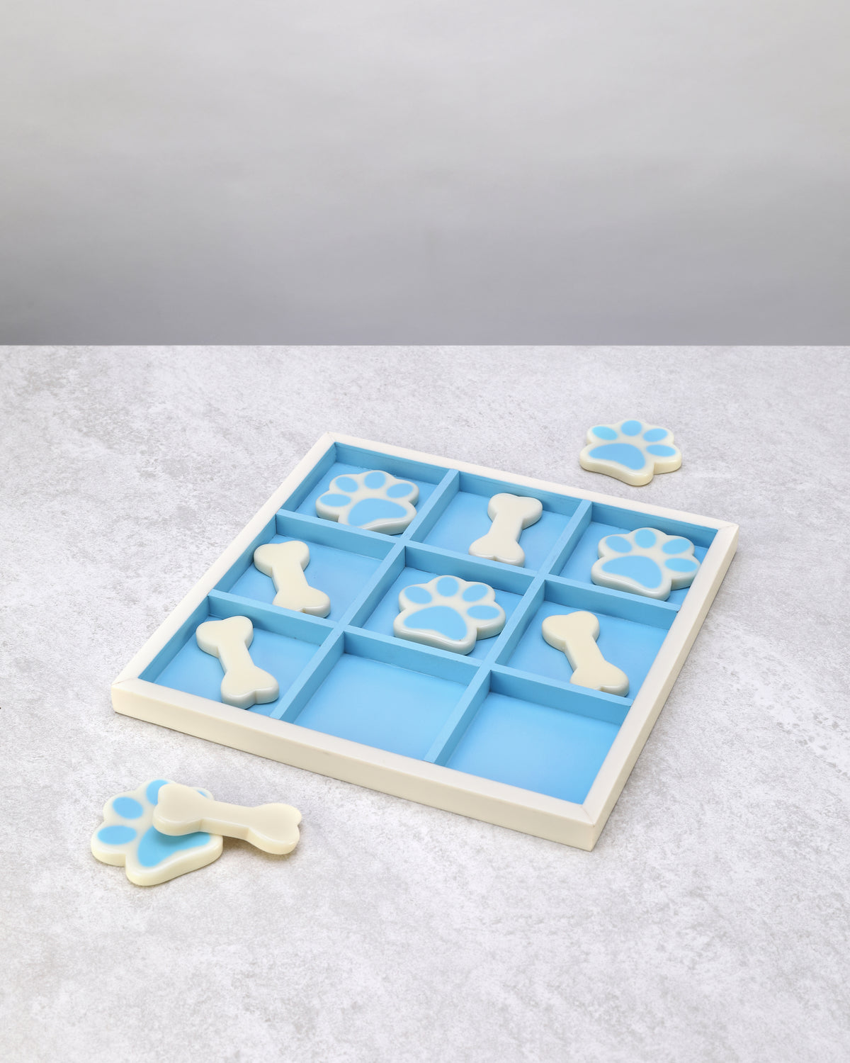 Resin tic-tac-toe board with spare bone and paw pieces beside it, angled view