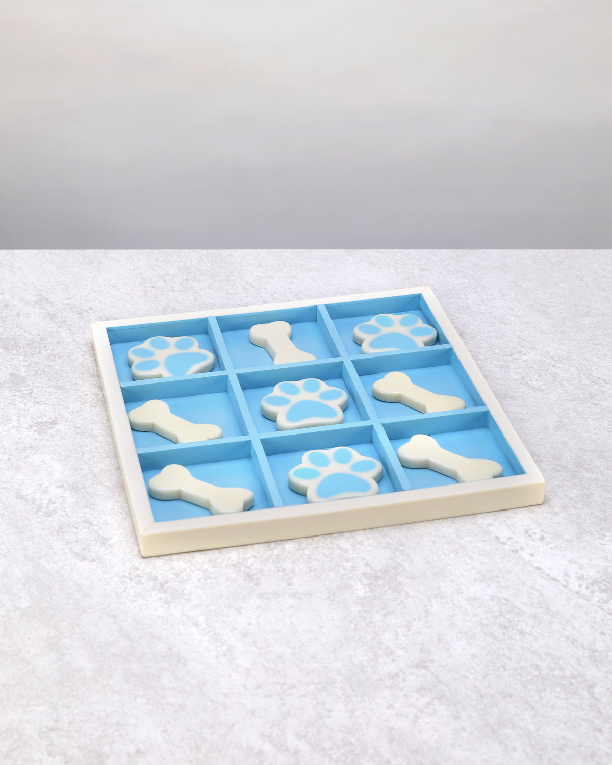 Blue and white resin tic-tac-toe board with bone and paw-print pieces, top view