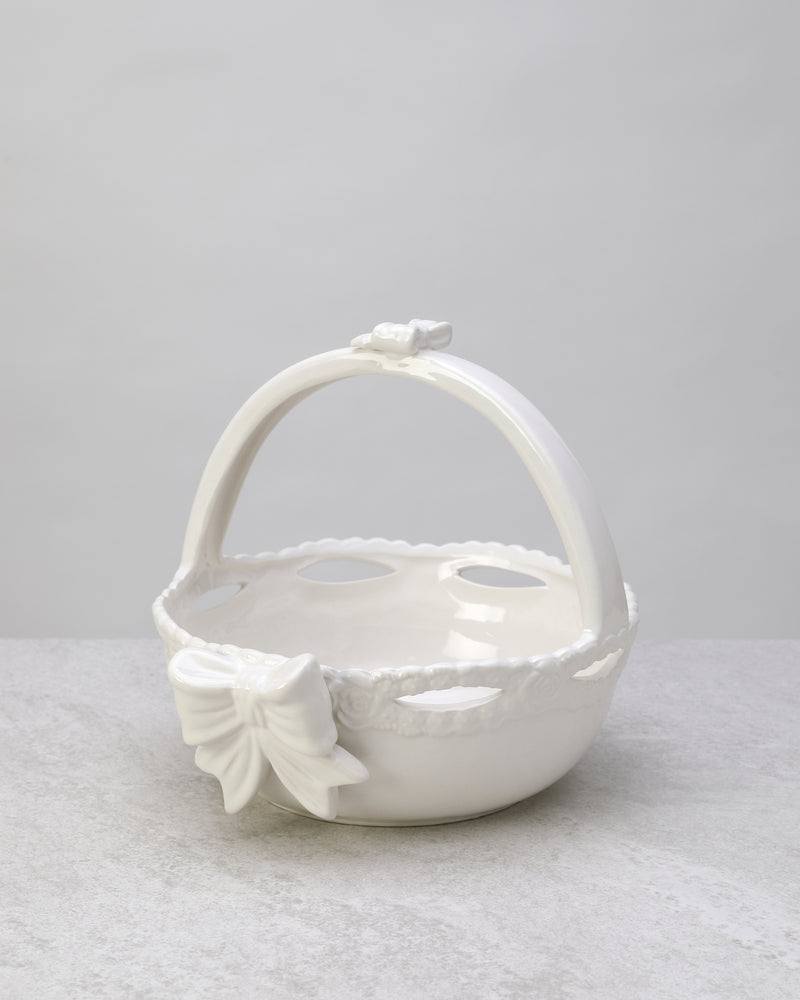 White glazed ceramic basket with an arched handle and a bow detail, on white