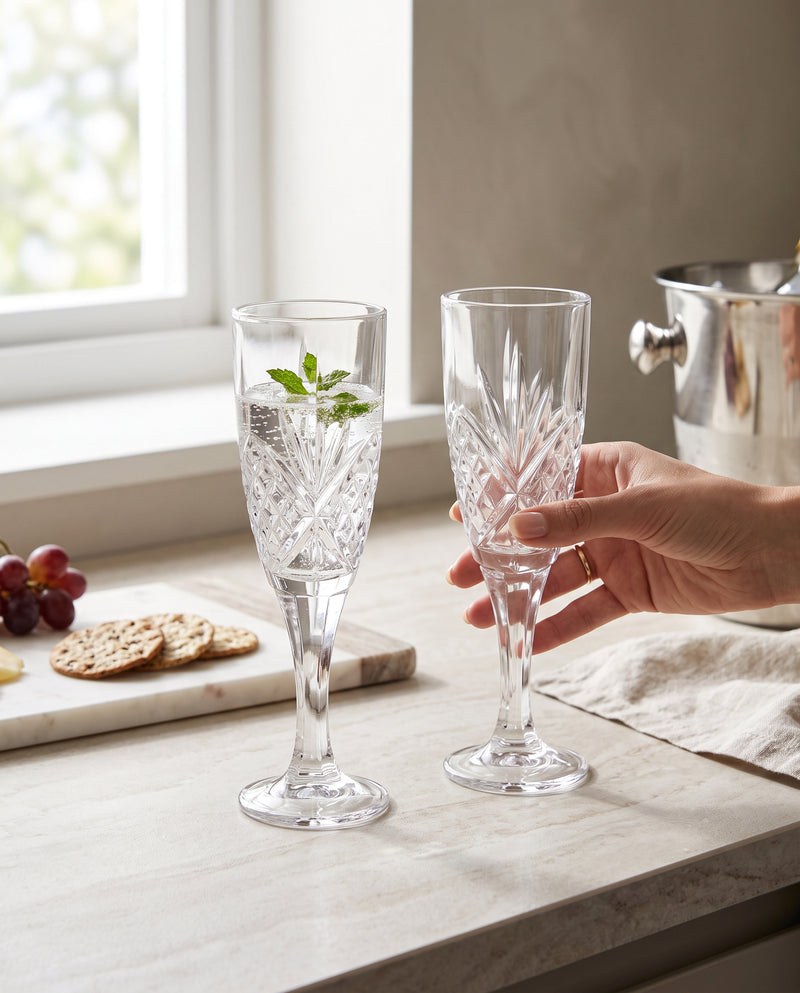 Hands toasting with clear machine cut champagne flutes at a table