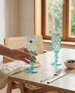Aqua champagne flutes on a dining table by a window, a hand holding one